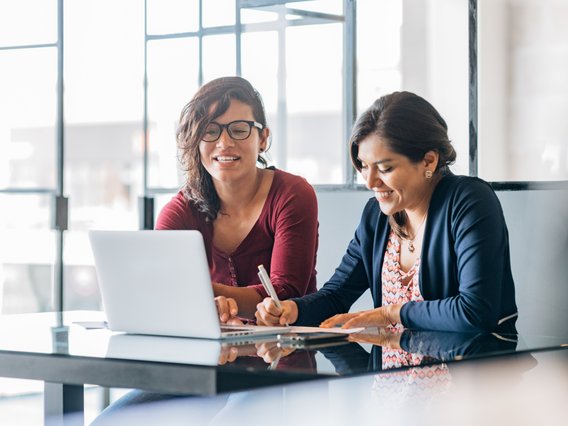 arbeitssituation-gespräch-schreibtisch-laptop-fröhlich Mitarbeitende arbeiten gemeinsam an einem Schreibtisch mit Laptop