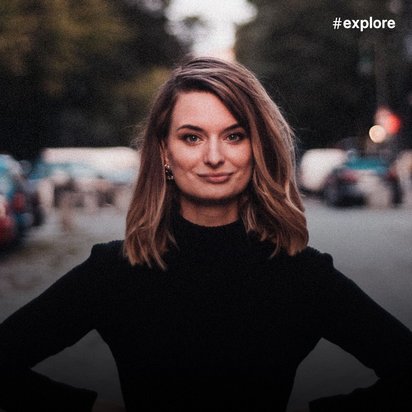 Maggie Herker mit schulterlangem braunen Haar und schwarzem Oberteil steht selbstbewusst auf einem Parkplatz oder einer Straße, im Hintergrund sind verschwommen geparkte Autos und gedämpfte Lichter zu sehen.