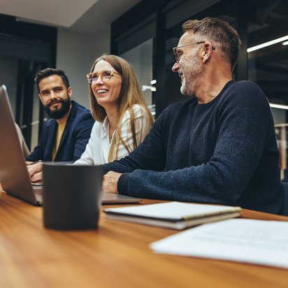 Kolleginnen und Kollegen sitzen bei einem Meeting und lachen zusammen.